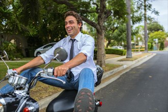 Hispanic businessman driving moped on neighborhood road