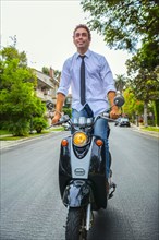 Hispanic businessman standing on scooter on neighborhood road