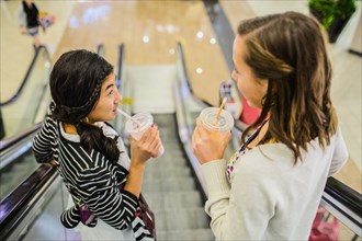 Girls drinking smoothies on escalator at shopping mall