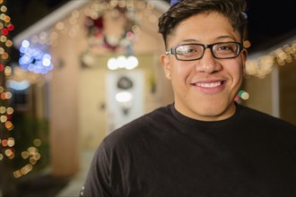 Hispanic man smiling outside house decorated with string lights