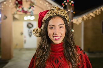 Hispanic woman smiling outside house decorated with string lights