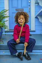 Pacific Islander boy with drumsticks sitting on front stoop