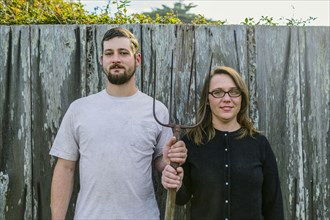 Caucasian couple holding pitchfork near fence