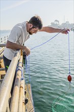 Caucasian man crabbing with net on wooden pier