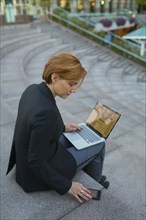 Caucasian businesswoman using cell phone and laptop in city park