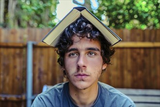 Hispanic man balancing book on head in backyard