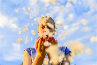 Caucasian teenage girl blowing flower petals under blue sky
