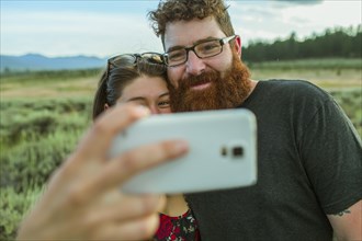 Caucasian couple taking selfie with cell phone in remote field