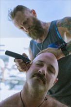 Caucasian man shaving head of friend