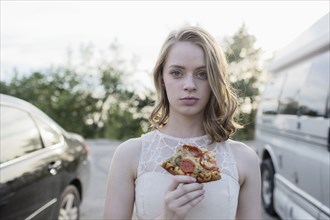 Caucasian teenage girl eating pizza in parking lot