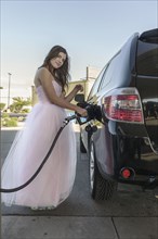Caucasian girl wearing prom dress fueling car