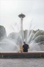 Caucasian man and dog sitting on fountain near tower