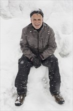 Smiling Caucasian man sitting on pile of snow