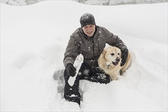 Caucasian man sitting in snow hugging dog