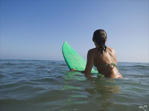 Hispanic girl sitting on surfboard