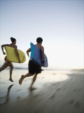 Multi-ethnic couple running with surfboards