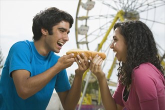 Multi-ethnic couple eating hot dog at carnival