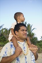 Pacific Islander father with son on shoulders at beach