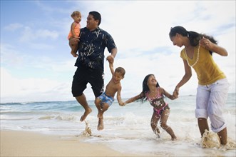 Pacific Islander family jumping in ocean surf