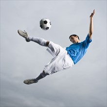 Mixed race teenager in mid-air kicking soccer ball