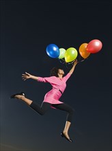 African woman holding bunch of balloons in mid-air