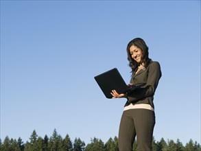 Mixed race businesswoman using laptop outdoors