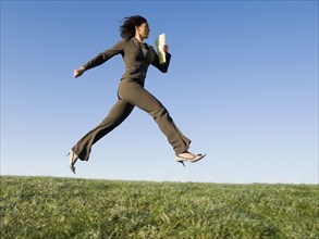 Mixed race businesswoman leaping in field