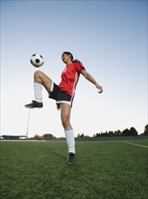 Mixed race woman bouncing soccer ball on knee