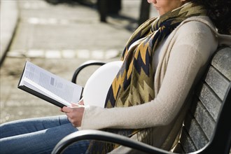 Pregnant Middle Eastern woman reading on park bench