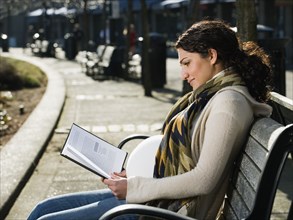 Pregnant Middle Eastern woman reading on park bench