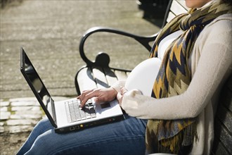 Pregnant Middle Eastern woman using laptop on park bench