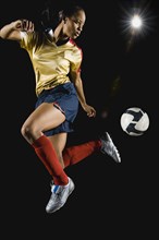 Mixed race soccer player kicking ball in mid-air