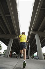 Mixed race man running under freeway overpass