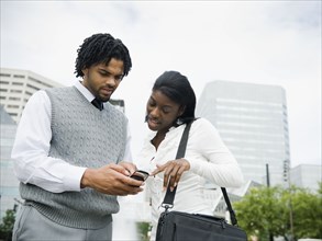 Businessman and businesswoman looking at cell phone in city