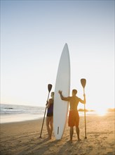 Couple standing on beach with surfboard and paddles