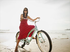 Hispanic woman riding retro bicycle on beach
