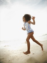 Mixed race girl in bathing suit running on beach