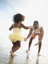 Black father bending to greet daughter on beach