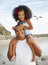 Black father carrying daughter on shoulders on beach