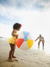 Black father throwing ball on beach with daughter