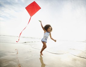 Mixed race girl running with kite on beach