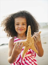 Mixed race girl holding starfish on beach