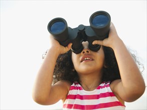 Mixed race girl looking through binoculars
