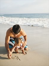 Mixed race father and daughter writing in sand together