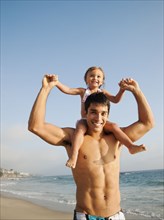 Mixed race father carrying daughter on shoulders