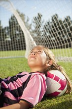 Hispanic girl soccer player laying with head on soccer ball