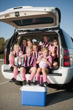 Girl soccer players sitting in back of car with trophy
