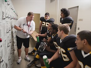 Coach talking to football players in locker room