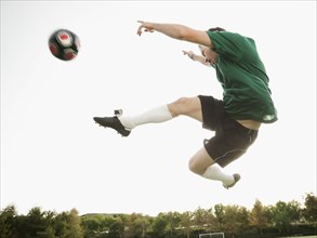 Caucasian soccer player in mid-air kicking soccer ball