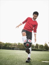 Asian soccer player practicing with ball on soccer field